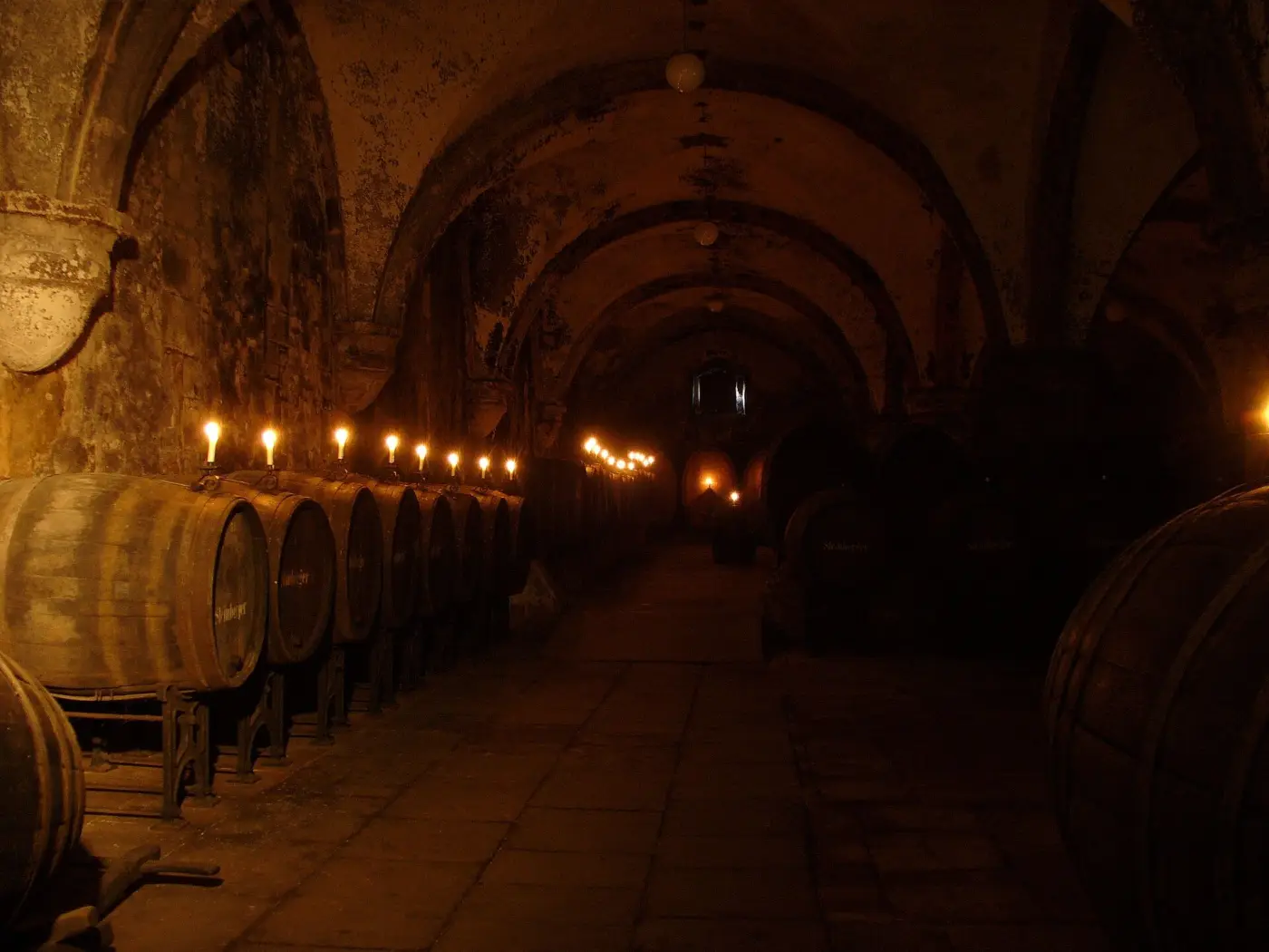 Cave voûtée éclairée à la bougie, tonneaux alignés le long du mur