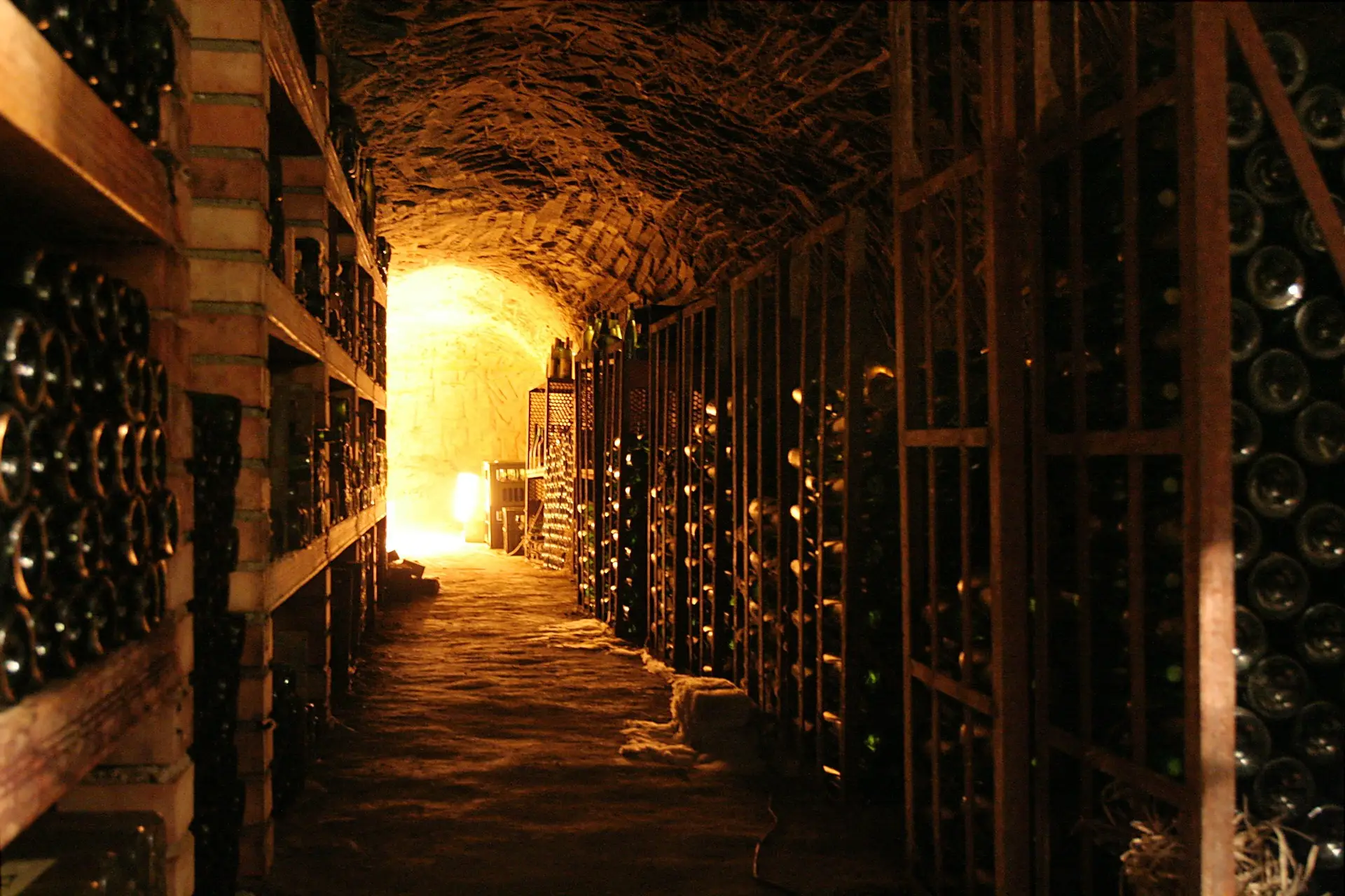 Galerie voûtée d’une cave à vin, casiers remplis de bouteilles baignés d’une lumière dorée